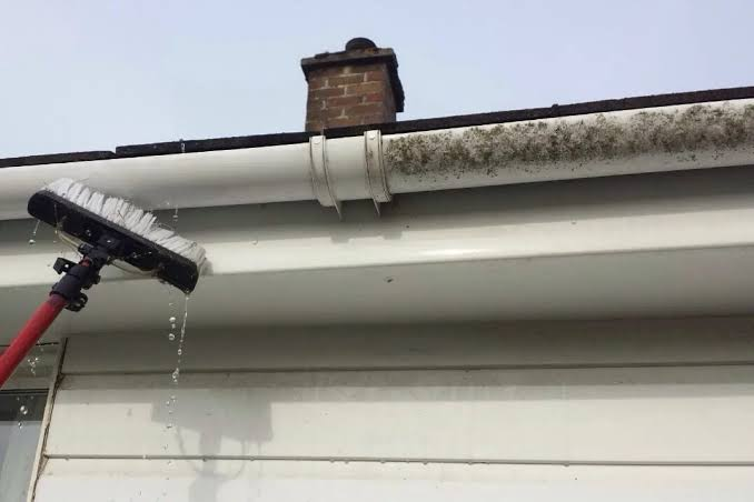 Exterior UPVC guttering being cleaned with a water-fed brush